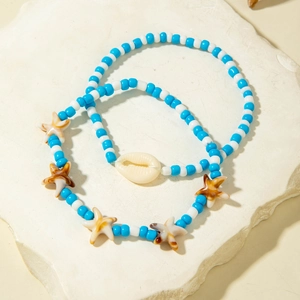 Blue and white beaded ocean anklet set with shell and starfish charms on a stone surface