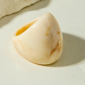 Macro shot of chunky acrylic ring with cream and amber marble texture on stone backdrop