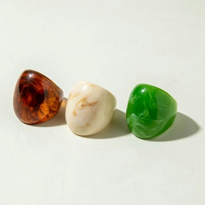 Close-up of chunky acrylic resin rings in amber, marble, and emerald green finishes