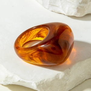 Close-up of amber acrylic oval ring with smoky texture on a natural stone base