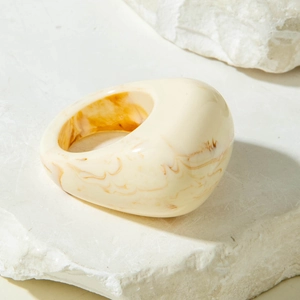 Macro shot of chunky cream resin ring with amber marble texture on white natural stone