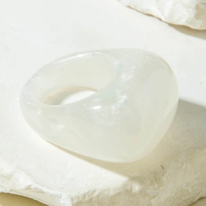 Detail of a minimalist white translucent acrylic ring on a textured stone surface
