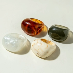 Detail view of four thick acrylic rings in amber, green, pearl white, and marble textures