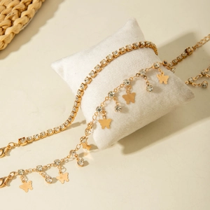 Close-up of golden layered anklets with crystal tennis chain and butterfly charms