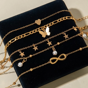Five-piece gold anklet set with butterfly, heart, star charms and pearls on a display