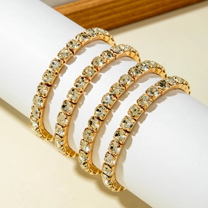Nahaufnahme von vier goldenen Tennisarmbändern mit quadratischen Kristallen auf weißem Ständer