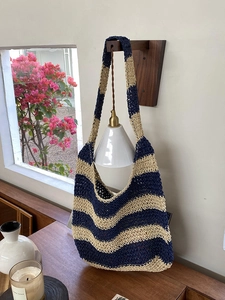 Detail of handwoven striped beach bag in navy and cream hanging on a wooden wall lamp