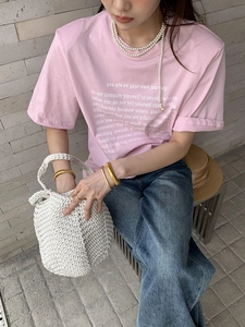 Close-up of a white hand-woven hollow shoulder bag paired with a pink cotton t-shirt
