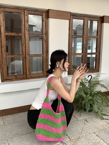 Detail view of pink and green striped handmade crochet shoulder bag on a model