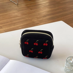 Pochette bijoux noire avec broderie cerise et fermeture éclair dorée sur socle blanc