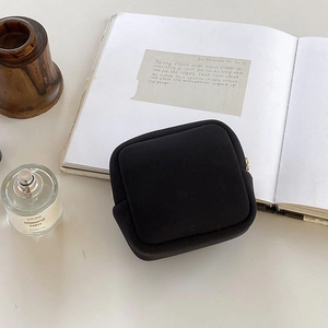 Pochette bijoux carrée noire minimaliste avec fermeture éclair dorée sur bureau blanc