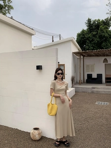 Outdoor shot of a model carrying a yellow hand-woven beach bag with a beige knit dress