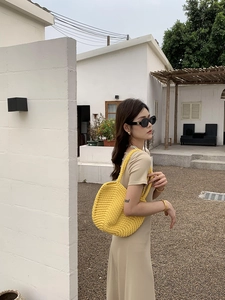 Outdoor shot of a bright yellow hand-woven crochet tote bag paired with a beige summer dress