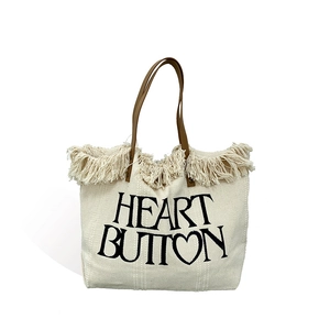 Minimalist canvas tote bag with fringes and brown leather straps featuring HEART BUTTON print