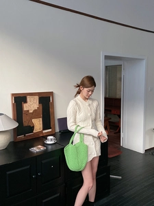 Detail of a bright green hand-woven chunky knit shoulder bag paired with a white cardigan