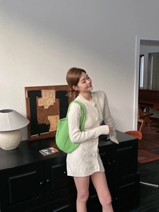 Detail of hand-woven cream cable-knit cardigan paired with vibrant green crochet handbag