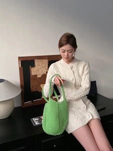 Close-up of a handwoven hollow straw green handbag paired with a knitted cardigan dress
