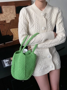 Close-up of bright green handmade woven bag with white cable-knit cardigan texture