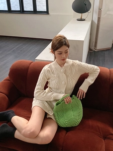 Detail of a large hand-woven green shoulder bag styled with an ivory cable knit cardigan
