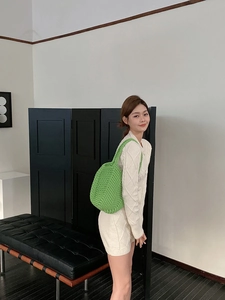 Detailed view of hand-woven green crochet shoulder bag worn by model on white knit dress