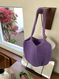 Detail of hand-woven purple crochet tote bag with textured knit pattern on a wall hook