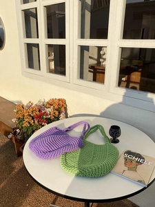 Close-up of hand-woven purple and green knit bags with thick cotton texture in warm sunlight
