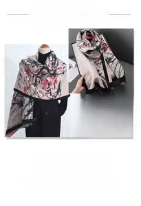 Close-up of red plum blossom print and fringe details on a warm beige winter scarf