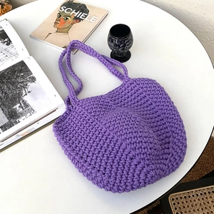 Purple handmade crochet shoulder bag with open semi-circular design on a white table