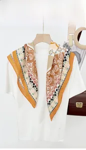 Detail of paisley pattern square scarf with orange borders on a wooden hanger