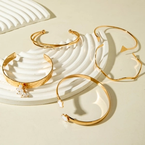 Ensemble de 5 bracelets dorés avec motifs trèfle et perles sur socle blanc