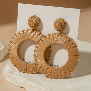 Detail of bohemian woven raffia hoop earrings with golden beads on a textured base