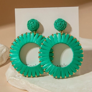 Close-up of green raffia woven hoop earrings with gold bead trim for a boho vacation look