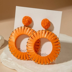 Bohemian large orange raffia hoop earrings with gold beads on a minimalist display