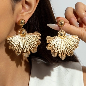 Detail of fan-shaped raffia earrings with golden metal base in a bohemian style