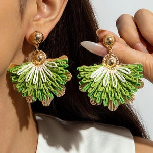 Close-up of bohemian raffia woven fan earrings with green and cream fibers