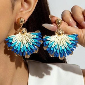 Close-up of bohemian colorful raffia fan-shaped earrings worn by a model for vacation