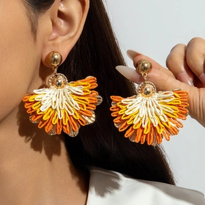Detail of fan-shaped raffia earrings in orange and yellow on model with close-up view