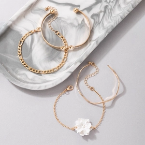 Detail of four-piece gold jewelry set including layered bracelets and camellia flower charm
