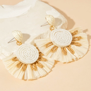 Close-up of bohemian fan-shaped raffia flower earrings on a white stone pedestal