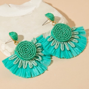 Close-up of emerald green raffia fan earrings with handmade beadwork and summer tassels