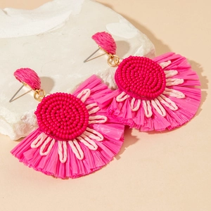 Detail of rose pink bohemian raffia earrings with beaded texture on a stone background