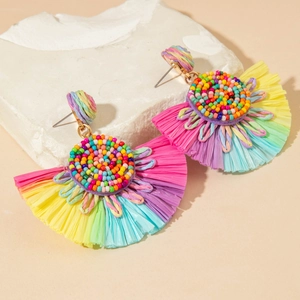 Detail view of colorful raffia fan-shaped earrings with beads on white stone pedestal