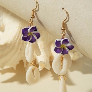 Detail of purple frangipani flower earrings with white shells on a textured background