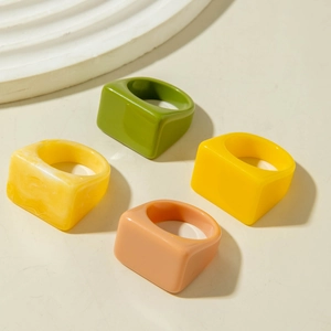 Vista macro de cuatro anillos acrílicos geométricos en tonos verde, amarillo y rosa