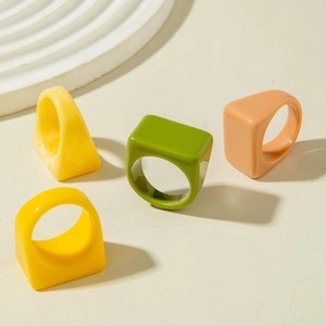 Juego de cuatro anillos de resina de colores amarillo verde y rosa sobre fondo beige