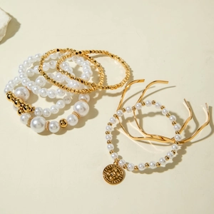 Elegant multilayered gold bracelet set with pearls and a round charm on soft background