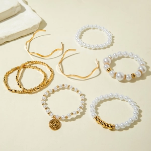 Elegant 7-piece layered bracelet set with gold bangles and pearls on neutral background