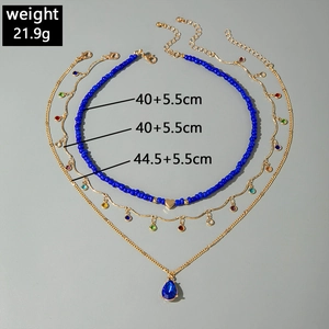 Close-up of triple-layered gold chain necklace with blue teardrop gem and heart bead