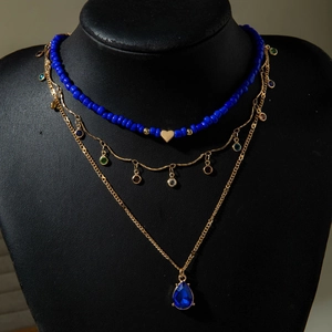 Three-layer gold necklace set featuring blue teardrop pendant and beaded heart chain