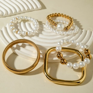 Detailed close-up of 5pcs gold metal bracelets and white pearl stack on a white pedestal